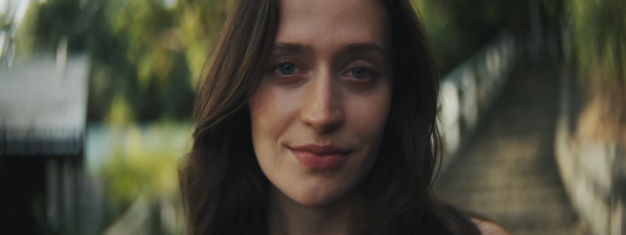 A womans face with green eyes looking forward and behind her is a staircase with concrete steps