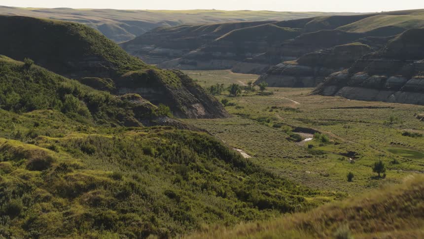 A valley is visible behind a grassy ridge in the badlands during summer