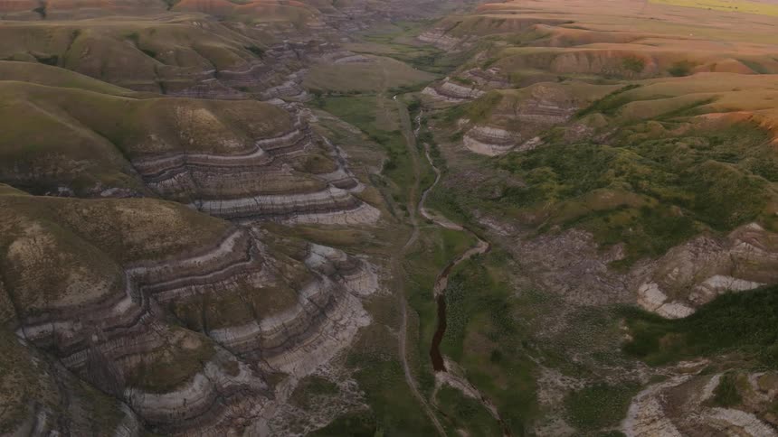 A small river winds through a grassy badlands canyon at dusk