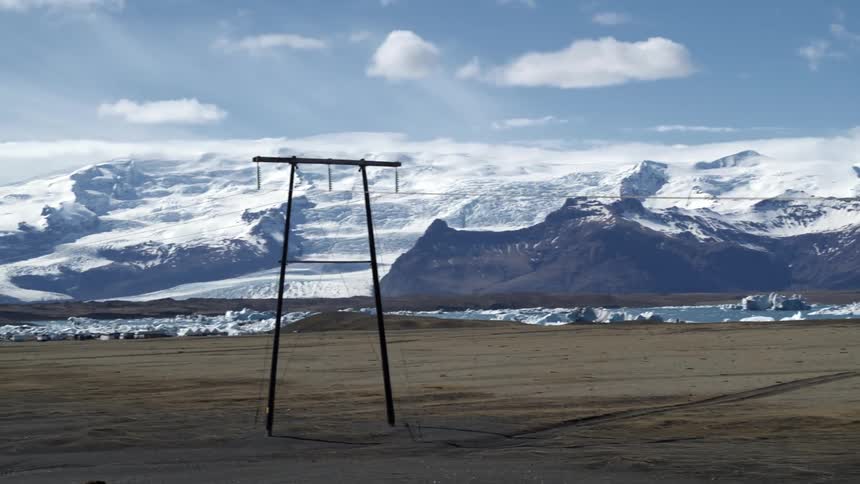 Aerial view of a power transmission pole with snowy mountains and icebergs around