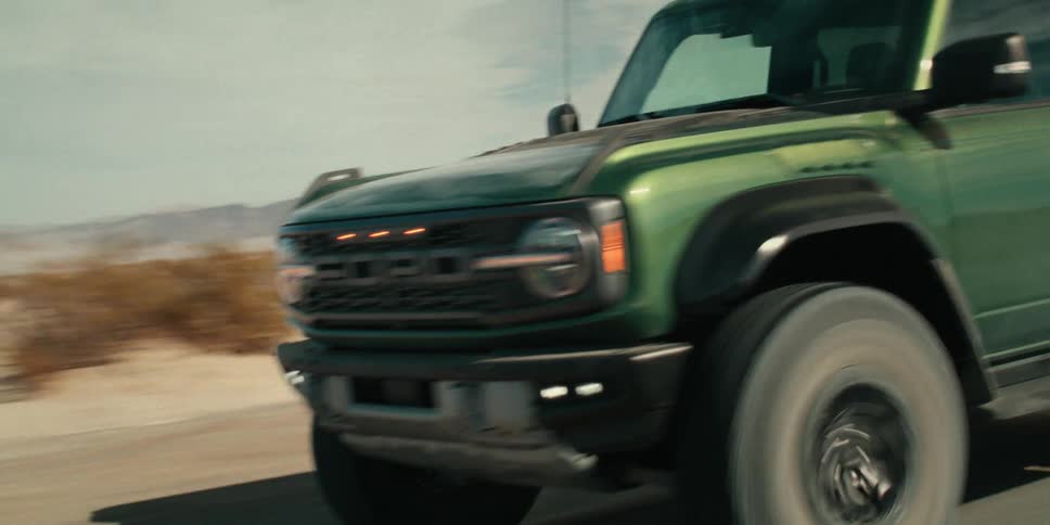 A green ford bronco drives down a road in a desert landscape
