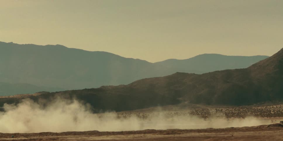 Car traveling on a dirt road releasing dust with mountains around