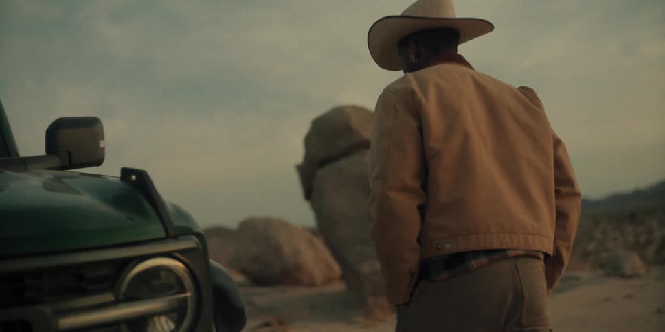 Man from behind walking next to his car with a hat and being in a deserted environment