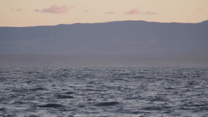 Ocean water is moving while the sun is setting above it