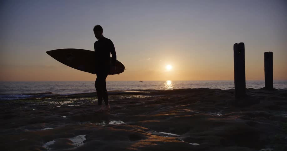 A male surfer walks along a beach carrying his surfboard