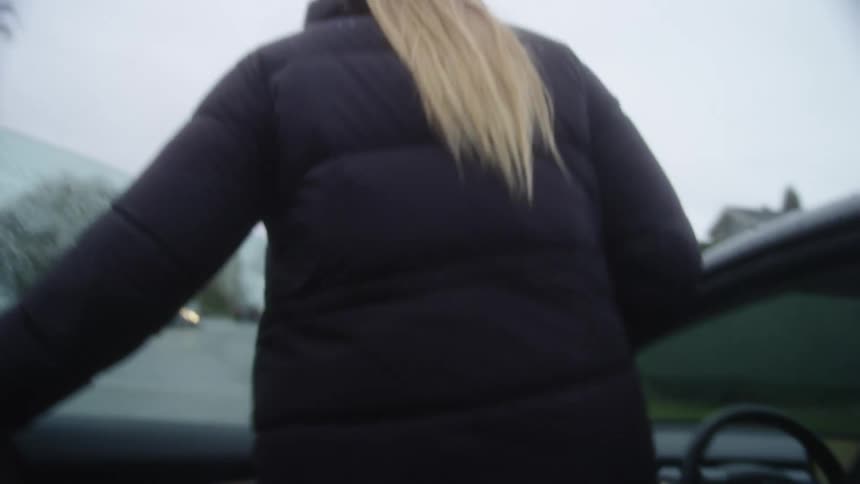 A woman walks up to a car and gets in