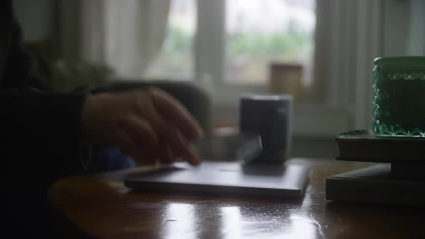 Person sitting indoors and closing their laptop shut