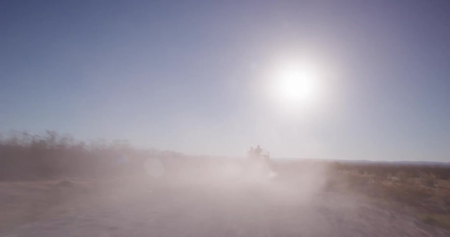 A vehicle drives on a dirt road kicking up dust