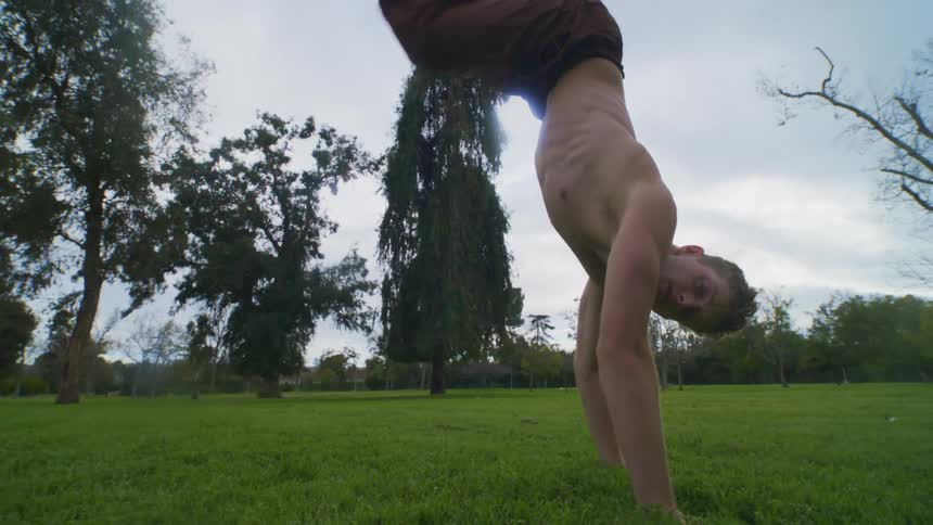 Shirtless male dancer balances on one hand in a field on a cloudy day