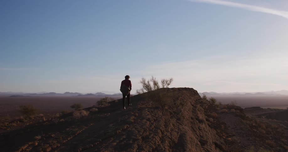 A person walking on the ridge of a mountain in the desert at morning