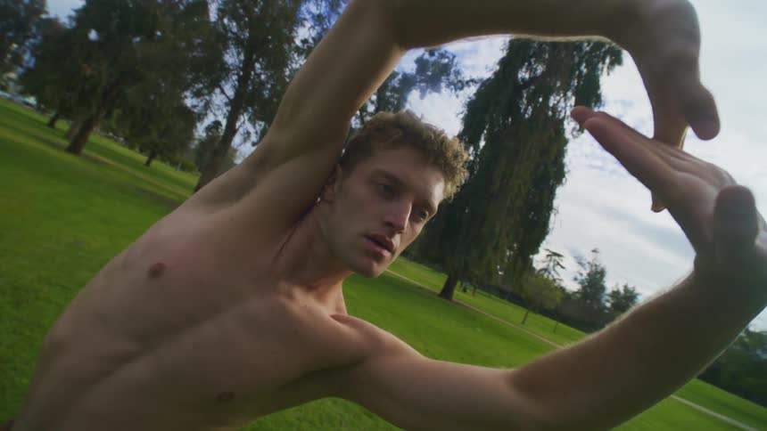 Shirtless man outdoors dancing and making hand gestures