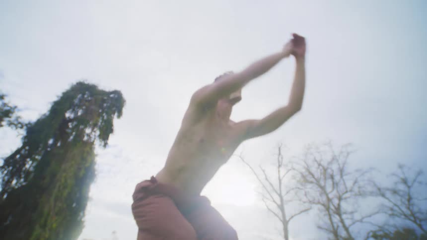Man without a shirt and in an openair park on a cloudy day jumping and dancing