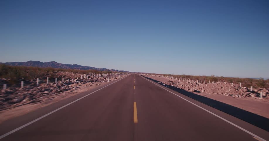 An empty road in the middle of a rural area on a clear sky day