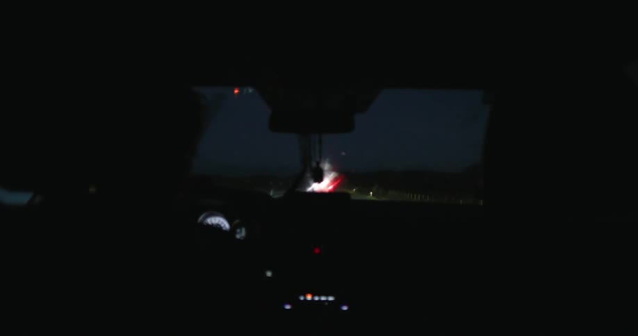 Silhouette of a person driving with a view of the dashboard and windshield of a car along the road at night