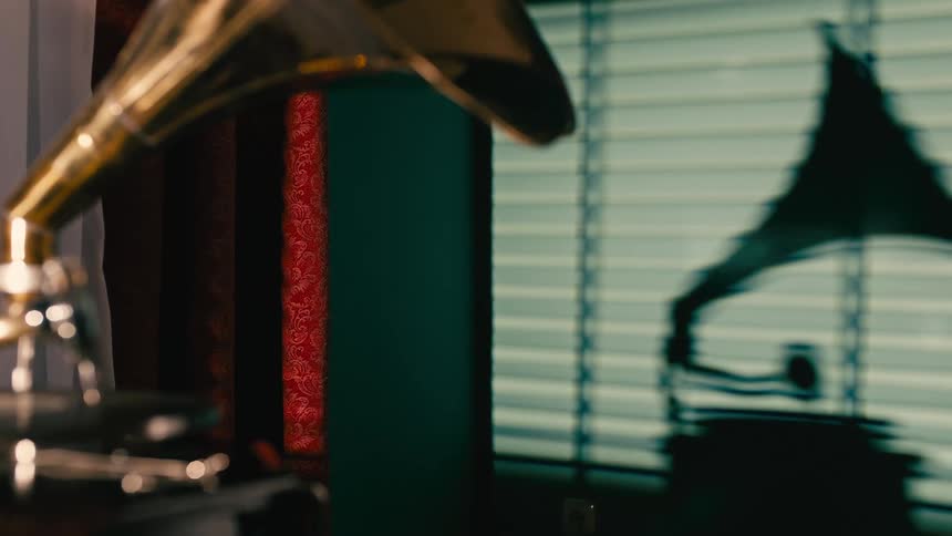 Person casts a shadow on window while moving needle off the record on the gramophone