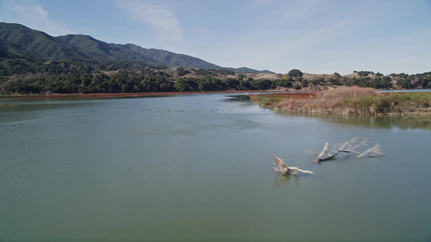 Aerial scenery of a river with birds flying and mountains around