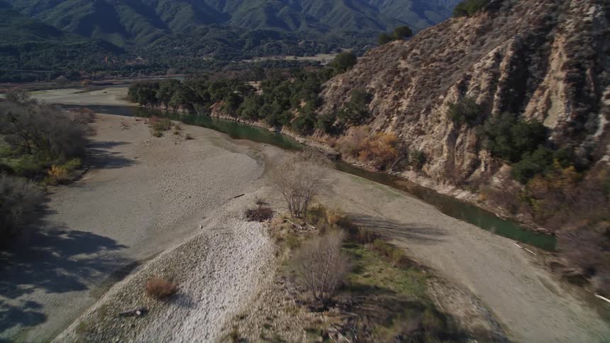 Aerial view of a river on an arid landscape next to lush green mountains