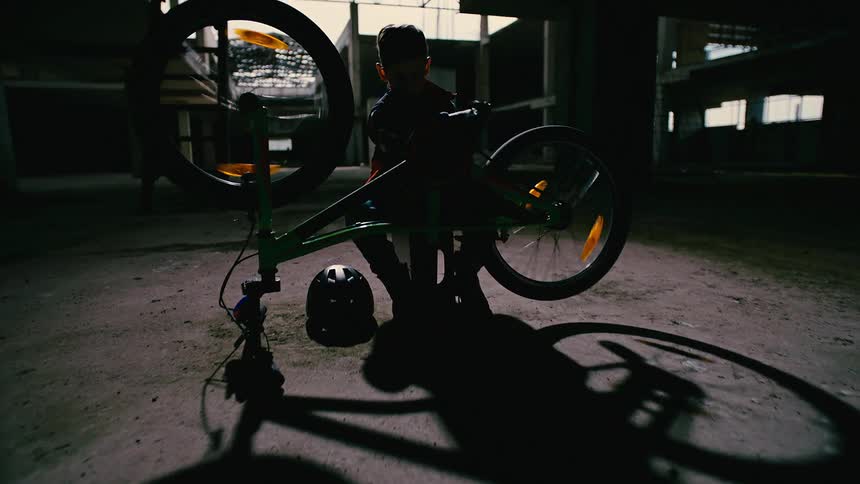 A young boy fixes his bicycle inside an abandoned building