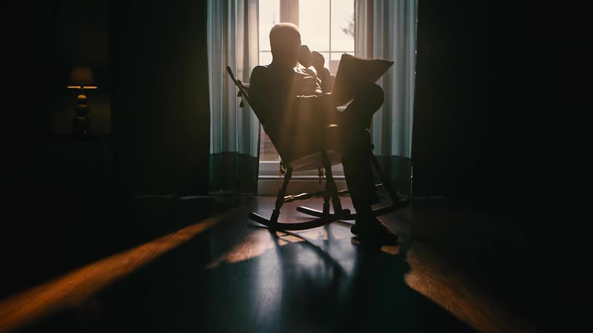 Silhouette of a man sitting on a rocking chair reading newspapers