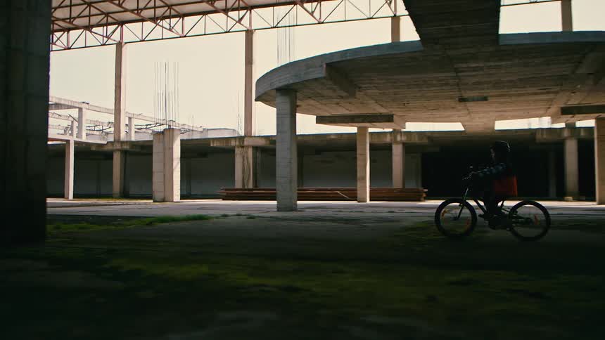 Little boy riding a bicycle in an abandoned building during the day