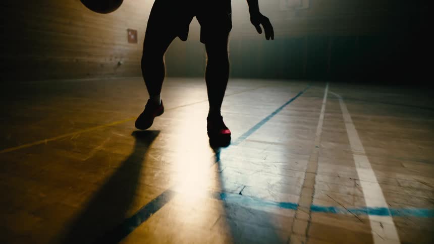 A man is performing a crossover dribble with a basketball while moving backward
