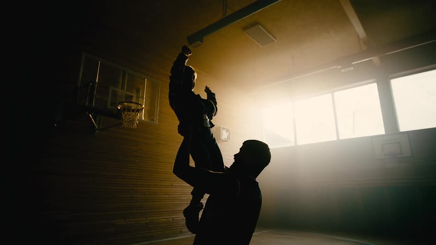 A father lifts his son on the basketball court
