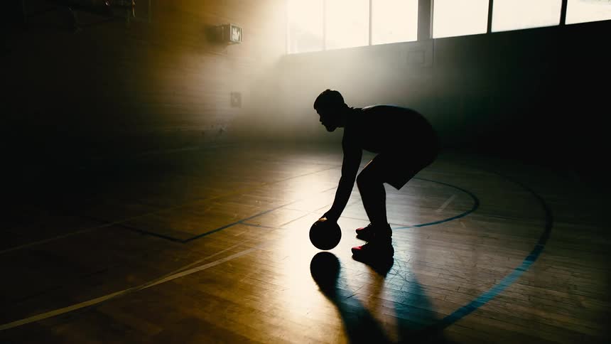 Silhouette of a man catching a ball and throwing it into the basket on a basketball court