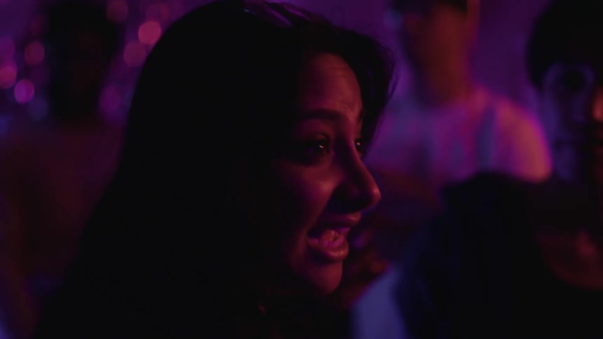 Close up of the face of a woman under purple lighting talking at a party