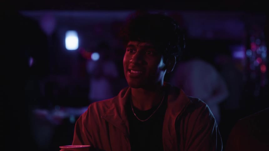 Young man converses with another person in a night club laughing and smiling as he speaks