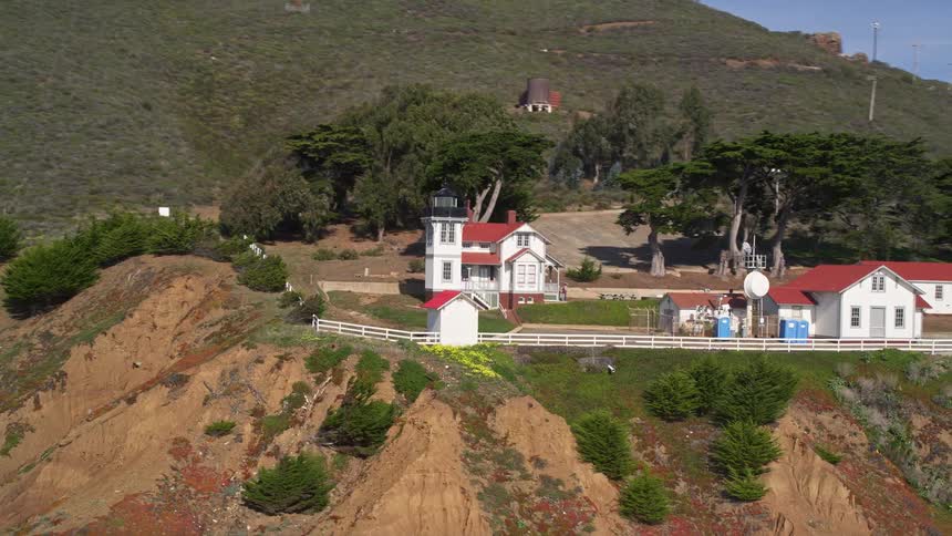 Drone view of a homes on a cliff overlooking waves crashing on rocky shoreline below