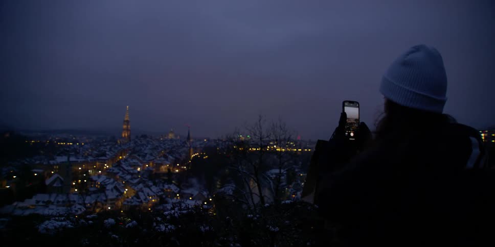 Woman uses her phone to record the view of the snow-covered city of Bern, Switzerland below her