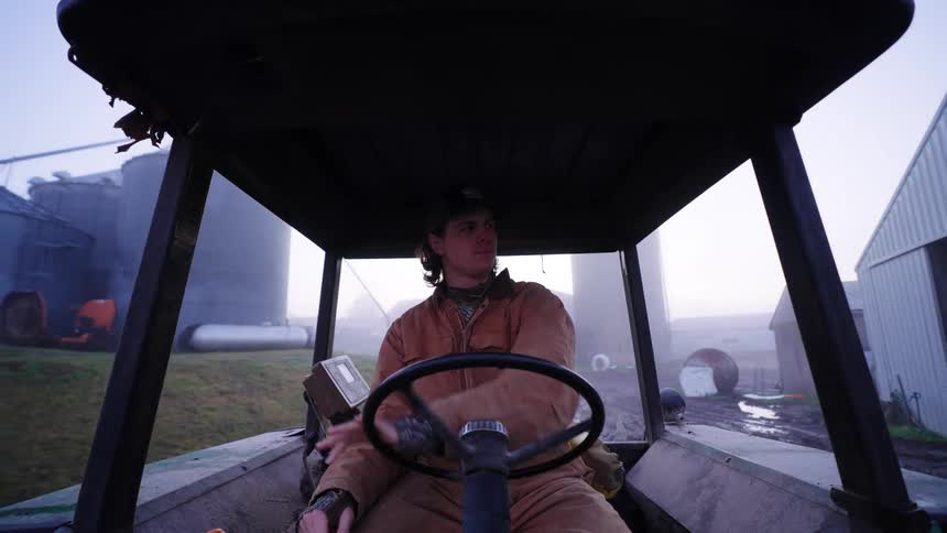 A man driving a tractor at a farm on a foggy morning