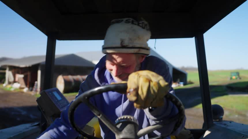 Man driving a tractor laughs while going over a bumpy road on his farm