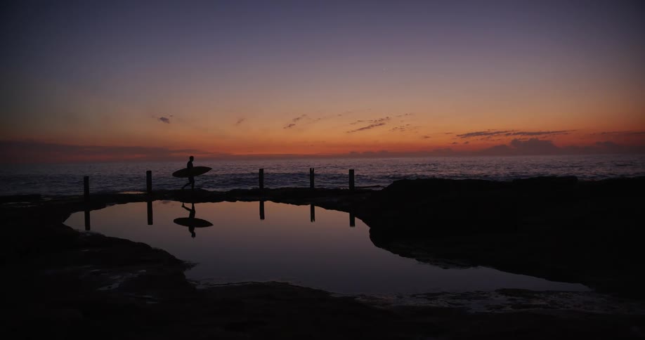 A person is walking on the beach while carrying a surfboard