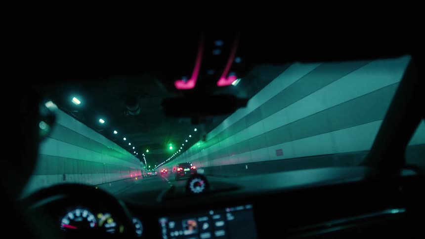 Inside view of the front windshield and dashboard of a vehicle traveling on an overpass at night in a metropolis