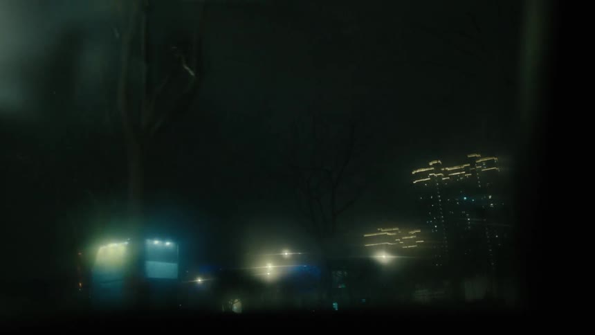 Footage of a city skyline at night seen through a dirty car window