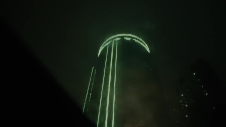 Upward view of the sunroof of a vehicle moving through a night metropolis with skyscrapers