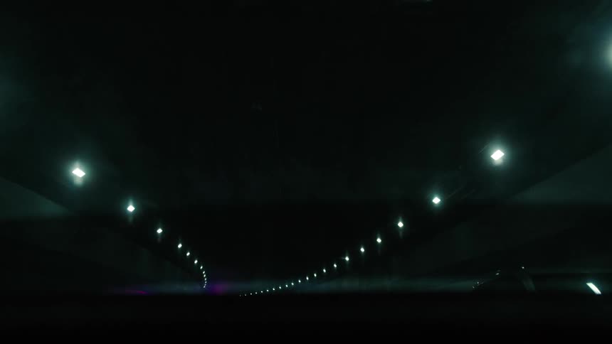 Vehicles drive along covered road lit by rows of electric lights on the ceiling