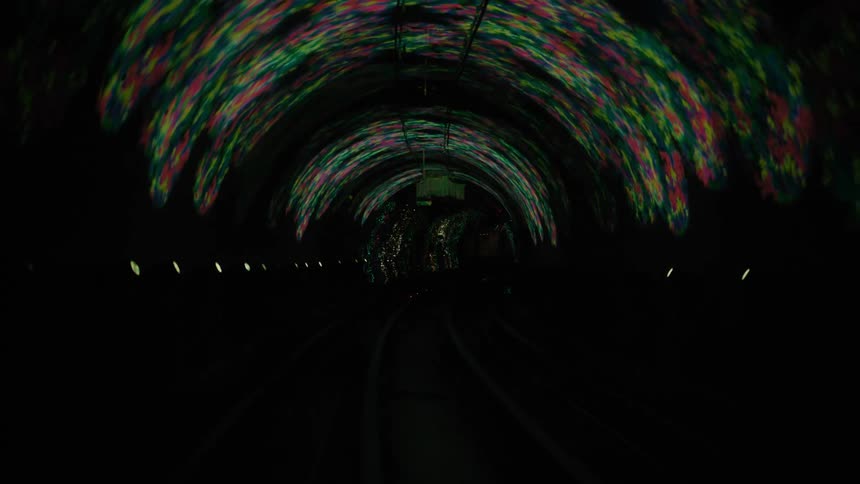 Colored lights form patterns on the arched ceiling of a long dark tunnel
