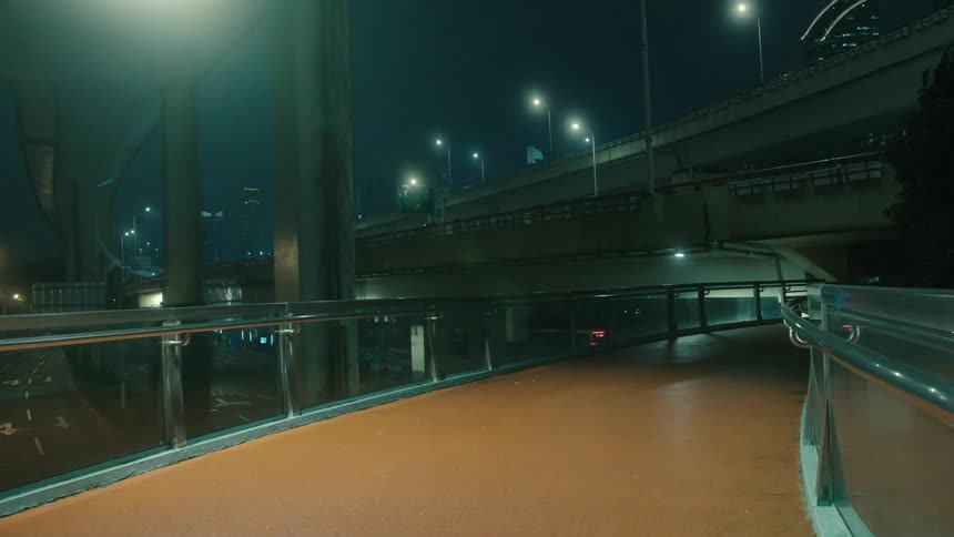 Point of view of a walkway next to an overpass with vehicle traffic in a metropolis at night