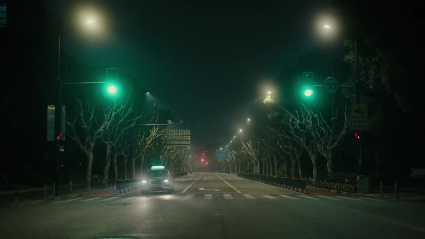 Street of a metropolis at night with a taxi passing after the traffic lights change