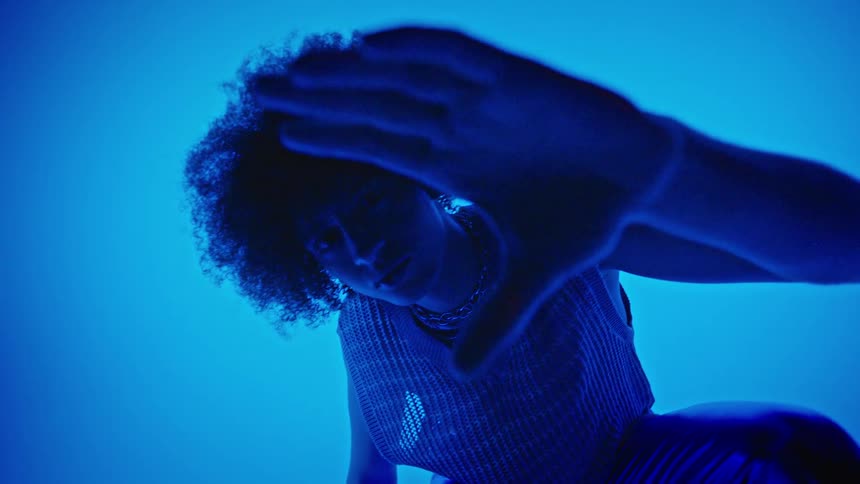 Man model crouching and making a hand gesture while standing in a studio with an electric blue light