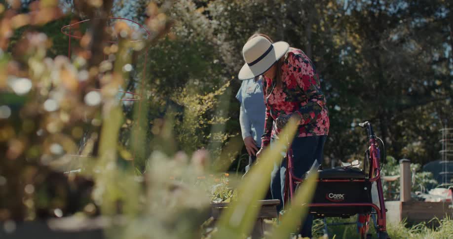 A nurse helps an elderly woman to tend her garden