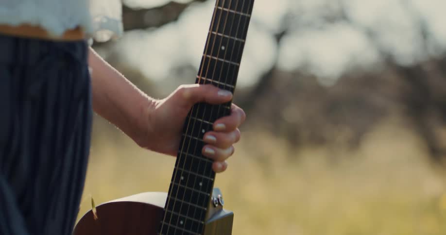 Hand of a woman walking in a field holding a guitar