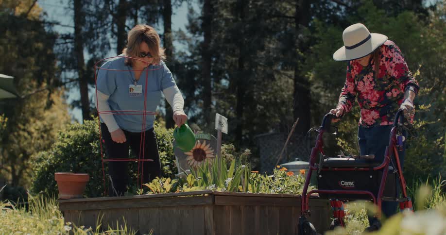 A healthcare worker waters an old womans garden