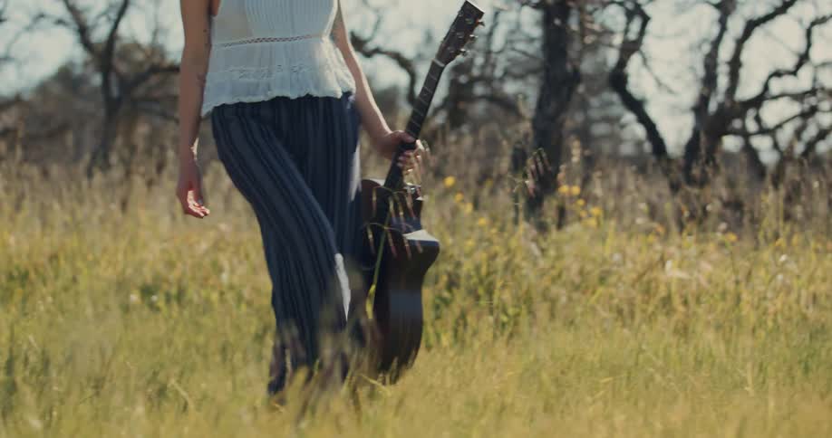 Woman walking in a natural field with a guitar in one hand