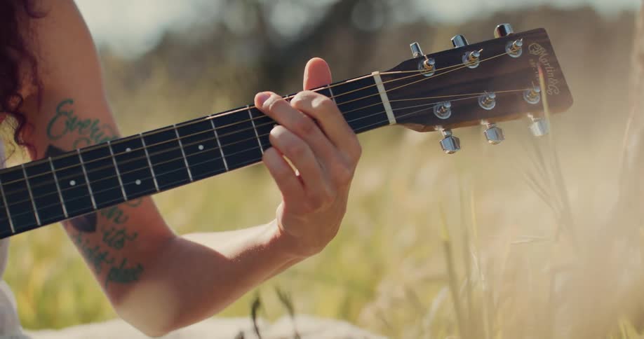 Hand of a woman playing the guitar while standing in a field with natural grass