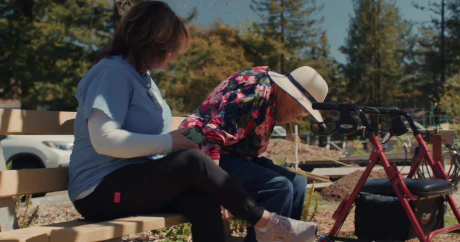 A nurse sits with an elderly patient on a bench in the garden