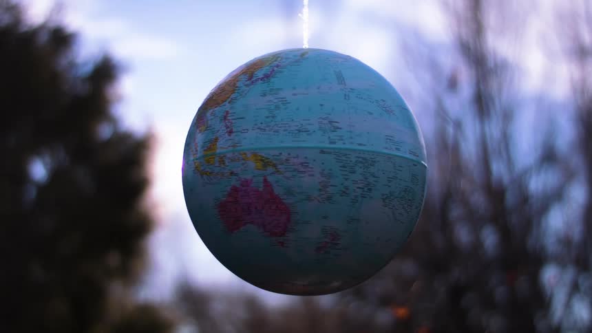 A hanging globe is illuminated by sunlight with trees and the sky in the background