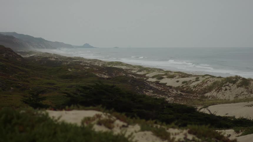 A beach with large waves rolling in towards the shore under an overcast sky